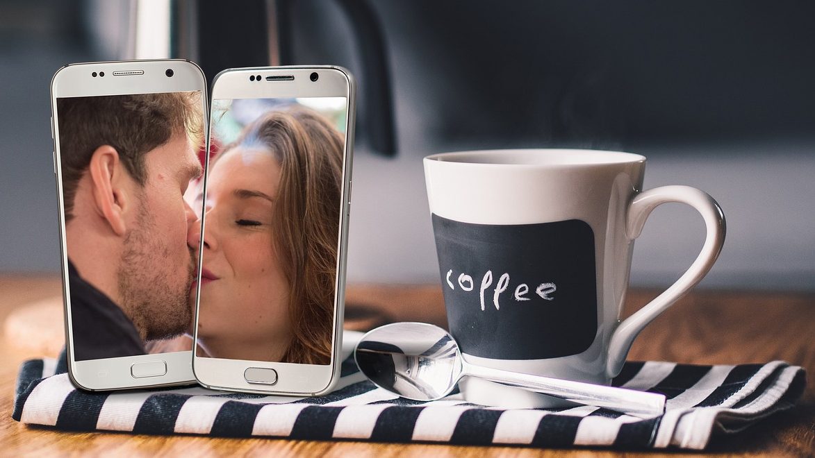 Deux amoureux en visioconférence, souriants, entourés d’objets ludiques comme des cartes de jeu et un téléphone
