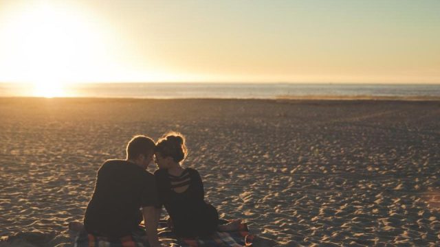 Un couple assis sur une plage au coucher du soleil