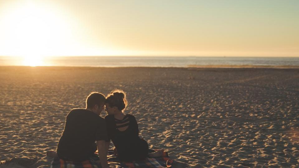 Un couple assis sur une plage au coucher du soleil